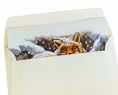 Une carte de vœux est glissée dans une enveloppe. La carte de vœux peinte à la main représente un renard couché dans la neige avec de gros flocons qui tombent. L'enveloppe est de couleur ivoire.