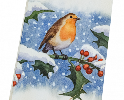 Carte de vœux peinte à la main représentant un rouge-gorge posé sur une branche de houx. Les feuilles et les baies du houx sont couvertes de neige. Le fond de la carte est bleue outremer avec des flocons de neige qui tombent.