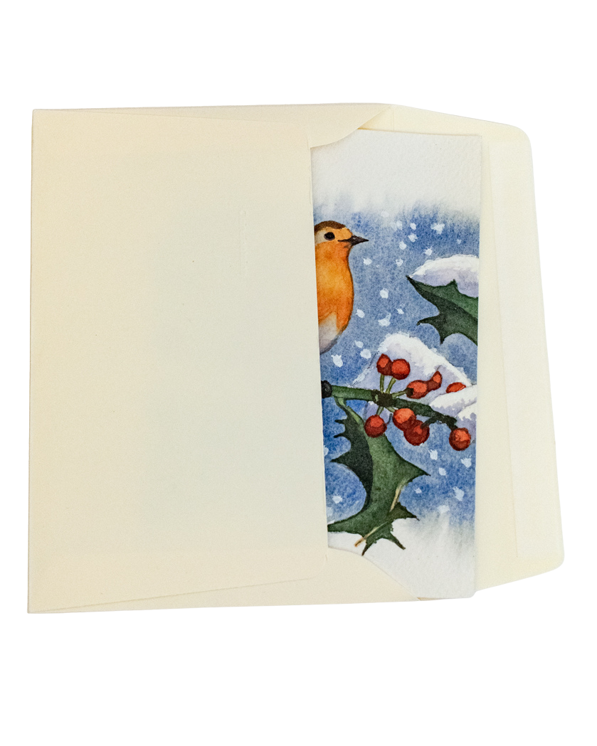 Une carte de vœux est glissée dans une enveloppe. La carte de vœux est peinte à la main et représente un rouge-gorge posé sur une branche de houx. Les feuilles et les baies du houx sont couvertes de neige. Le fond de la carte est bleue outremer avec des flocons de neige qui tombent. L'enveloppe est de couleur ivoire.